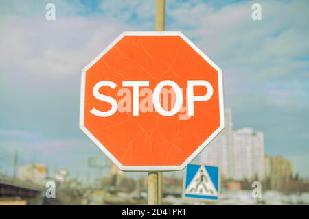 Stoppschild - Rot mit weißem Text mit blauem Himmel, Wolken, Gebäuden und Fußgängerüberweg Zeichen in backgournd. Stockfoto