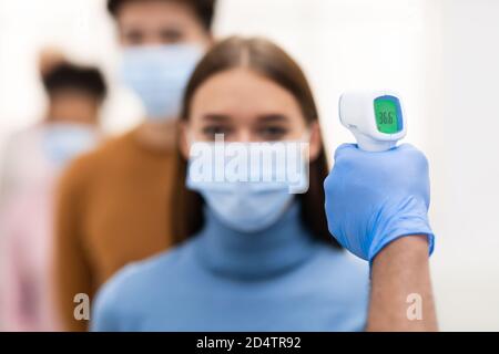 Medizinischer Arbeiter, Der Temperaturscreening Für Dame In Der Warteschlange In Innenräumen Macht Stockfoto