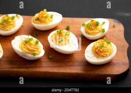 Hausgemachte Deviled Eier mit Schnittlauch auf einem rustikalen Holzbrett auf einer schwarzen Oberfläche, Seitenansicht. Nahaufnahme. Stockfoto