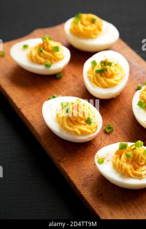 Hausgemachte Deviled Eier mit Schnittlauch auf einem rustikalen Holzbrett auf einer schwarzen Oberfläche, Seitenansicht. Nahaufnahme. Stockfoto