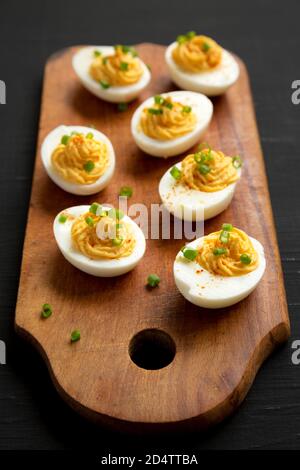 Hausgemachte Deviled Eier mit Schnittlauch auf einem rustikalen Holzbrett auf einem schwarzen Hintergrund, Low-Angle-Ansicht. Nahaufnahme. Stockfoto