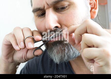 Ein bärtiger Mann schneidet vorsichtig seinen Schnurrbart mit einer kleinen Schere. Nahaufnahme. Stockfoto