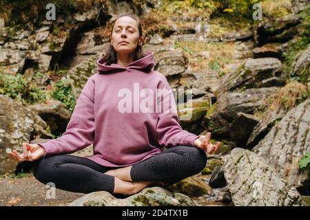 Friedliche junge Frau, die auf großen, gekreuzten Steinbeinen sitzt und meditiert Stockfoto