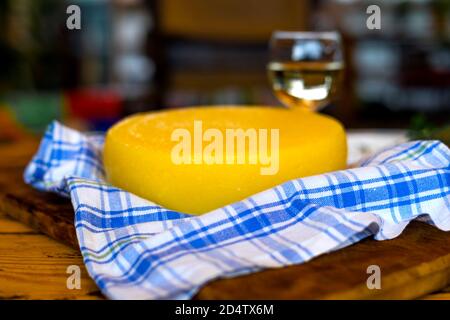 Käsekopf auf Holzbrett auf Holztisch serviert mit einem Glas Weißwein und Handtuch. Hausgemachter Käse. Food-Konzept. Geringe Schärfentiefe. Stockfoto