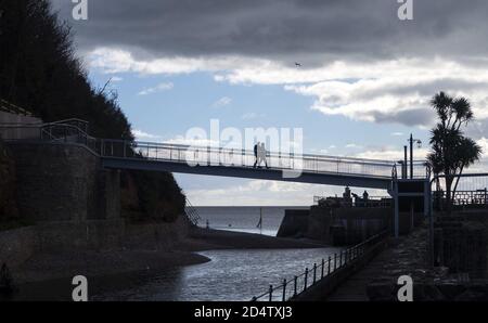 Sidmouth, Devon, 11. Okt 2020 Menschen überqueren die neu eröffnete Alma Bridge in Sidmouth, Teil des legendären South West Coastal Path. Die alte Brücke wurde geschlossen, da die Küstenerosion ihre Fundamente bedrohte, und die Arbeiten an der Ersetzung begannen im August 2019. Aufgrund der Coronavirus-Pandemie wurden die Arbeiten bis in diesem Frühjahr erheblich verzögert. Die neue Brücke überquert den Fluss Sid, und Bewohner und Wanderer können den südwestlichen Küstenweg ohne Umleitung ins Landesinnere fortsetzen. Kredit: Photo Central/Alamy Live Nachrichten Stockfoto