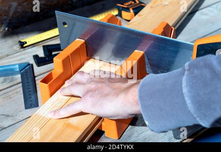 Mann schneidet eine Holzlatte mit einer Säge und Gehrungskasten. Nahaufnahme. Selektiver Fokus. Stockfoto