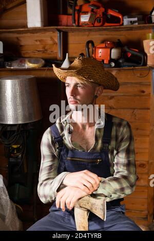 Junger Mann in den 20er Jahren trägt Latzhose und hält eine Axt. Stockfoto