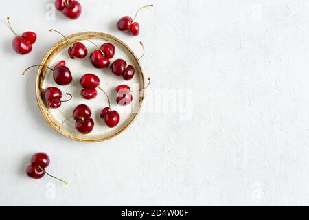 Hässliche rote Kirschen auf weißem Hintergrund auf Teller. Trendige Speisen in Form. Unvollkommene Bio-Beeren. Komposition aus der Nähe, Platz kopieren, für Text platzieren. Stockfoto