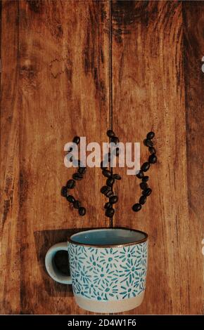 Kaffeetasse auf Holztisch, Kaffeebohnen auf Tisch in Dampfmuster. Draufsicht, vertikale Komposition. Stockfoto