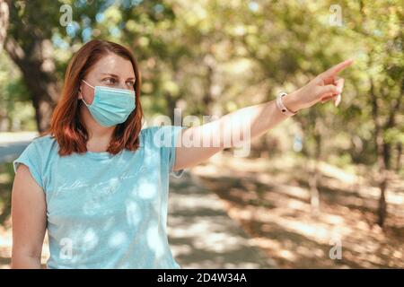 Coronavirus, covid 19. Kaukasische europäische Frau trägt eine Maske zur Verhinderung von Staub und Infektionen Virus Hand zeigt Richtung in den Stadtpark oder im öffentlichen Raum Stockfoto