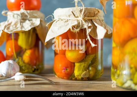 Hausgemachte Gläser mit eingelegten Tomaten und Gurken auf rustikalem Holzhintergrund. Eingelegtes und konservierte Produkt. Fermentierte Tomaten auf dunklem Hintergrund. Stockfoto