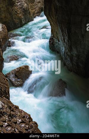 Stürmischer Gebirgsbach mit klarem blauen Wasser fließt eine felsige Schlucht in Partnachklamm in Deutschland hinunter. Sonnenlicht dringt von oben ein Stockfoto