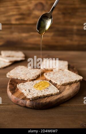 Crispbrea don einen Holzständer aus der Nähe. Honig wird aus einem Löffel auf den Cracker gegossen Stockfoto