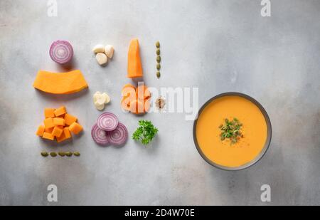 Herbst-Kürbissuppe in dunkler Schüssel und Zutaten zum Kochen. Stockfoto