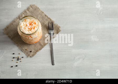 Hausgemachtes Sauerkraut im Glasgefäß auf weißem, hölzernen Hintergrund. Rote Beeren verziert. Behälter mit fermentierten Lebensmitteln stehen auf einer Segeltuch-Serviette mit Gabel. Stockfoto