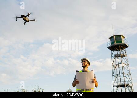 Arbeiter steht und prüft seine Pläne neben einem Flieger Drohne Stockfoto