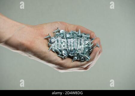 Schrauben in der Hand eines Mannes. Schrauben und Zahnräder. Werkzeuge zur Befestigung und Reparatur. Edelstahlschrauben. Verzinkte Metallbefestigungen. Stapel von Metallschrauben schließen Stockfoto