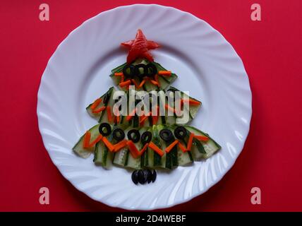 Silvester Essen. Weihnachtsbaum aus Lebensmitteln auf rotem Hintergrund. Neujahr. Kreative Idee, Konzept der vegetarischen und veganen Lebensmittel. Der Blick von oben, Stockfoto