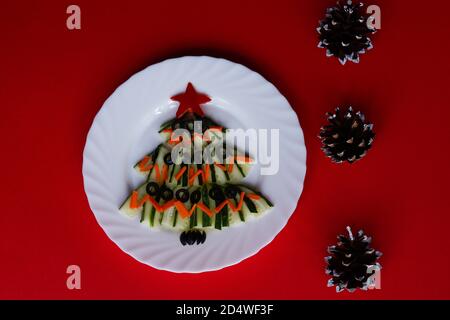 Silvester Essen. Weihnachtsbaum aus Gurkensalat auf rotem Hintergrund mit Zapfen. Schöne Weihnachten und Neujahr Essen Hintergrund Draufsicht auf Empt Stockfoto