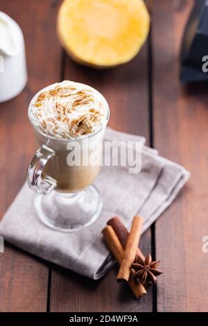 Kürbislatte, Milchkännchen und ein Stück Kürbis. Kürbislatte mit Schlagsahne und Gewürzen auf Holzbrettern. Heißer Herbstkaffee auf einem Laken-Nickerchen Stockfoto