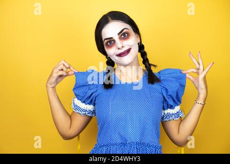 Frau trägt ein gruseliges Puppe halloween Kostüm auf gelbem Hintergrund Erfolgreicher Ausdruck Stockfoto