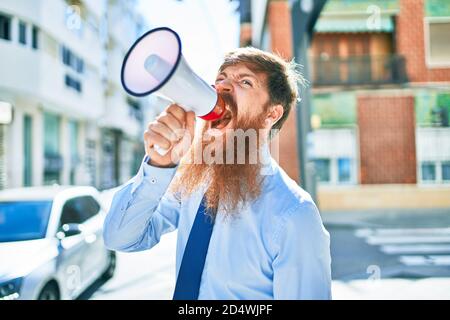 Junger rothaariger Geschäftsmann mit wütender Expression. Schreien mit Megaphon auf der Straße der Stadt. Stockfoto