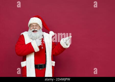 Glücklicher Weihnachtsmann zeigt Finger auf Kopie Raum Werbung auf rotem Hintergrund. Stockfoto