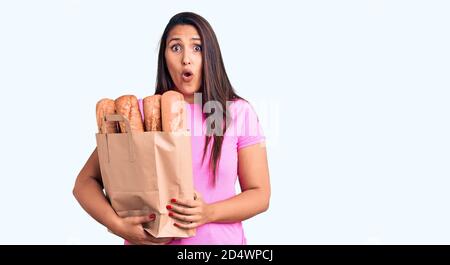 Junge schöne Brünette Frau hält Liefertasche mit Brot verängstigt und erstaunt mit offenem Mund für Überraschung, Unglauben Gesicht Stockfoto