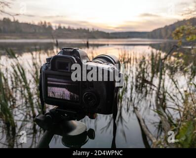 Schwarze Digitalkamera auf Stativ Aufnahme früh nebligen Morgen Landschaft Am Herbstsee mit selektivem Fokus Stockfoto