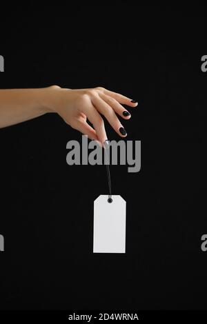 Frau Hand hält weißen Preisschild auf schwarzem Hintergrund. Stockfoto