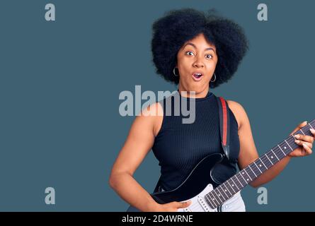 Junge afroamerikanische Mädchen spielen E-Gitarre erschrocken und erstaunt mit offenem Mund für Überraschung, Unglauben Gesicht Stockfoto