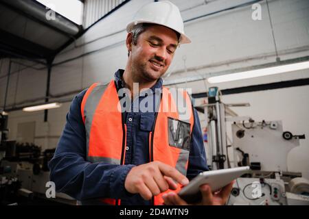 Nahaufnahme des kaukasischen Ingenieurs, der auf einem digitalen Tablet scrollt und recherchiert Techniken im Stand in der Fabrik Stockfoto