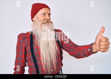 Alter älterer Mann mit grauem Haar und langem Bart trägt Hipster-Look mit Wollmütze sieht stolz aus, lächelnd tut Daumen nach oben Geste zur Seite Stockfoto