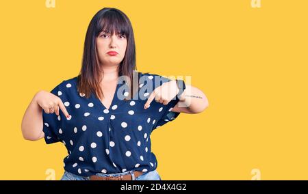 Junge plus size Frau trägt Freizeitkleidung nach unten schauen traurig und aufgeregt, zeigt Richtung mit den Fingern, unglücklich und deprimiert. Stockfoto