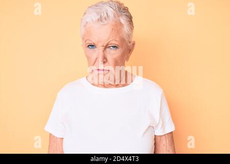Ältere schöne Frau mit blauen Augen und grauen Haaren tragen klassische weiße T-Shirt über gelben Hintergrund skeptisch und nervös, Stirnrunzeln aufgeregt wegen Stockfoto