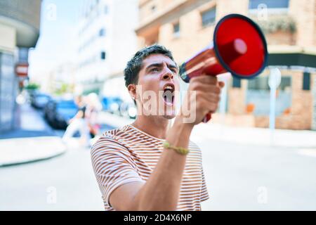 Junger hübscher kaukasischer Mann, der mit Megaphon in der Stadt schreit Stockfoto