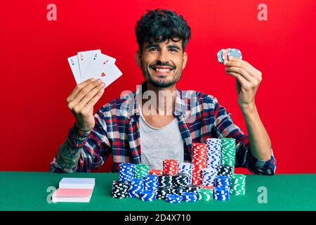 Junge hispanic Mann Poker mit Karten und Casino-Chips lächeln mit einem glücklichen und kühlen Lächeln auf Gesicht. Zeigt Zähne. Stockfoto