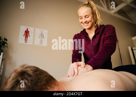 Weibliche Physiotherapeutin massiert männlichen Athleten liegend auf dem Bett in Pilates studio Stockfoto