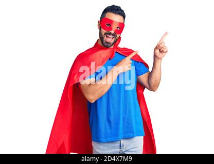 Junger hispanic Mann trägt Superhelden Kostüm lächelnd und schaut auf die Kamera mit zwei Händen und Fingern zur Seite. Stockfoto