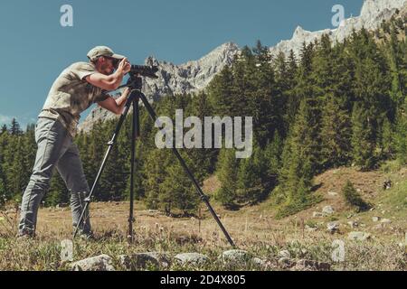 Kaukasischer Hobbyist Naturfotograf in seinen 40er Jahren, der mit Digitalkamera und Stativ in einem malerischen Alpenraum fotografiert. Stockfoto