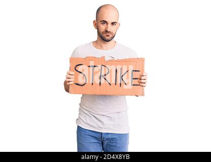 Junge gutaussehende Mann hält Streik Banner Denken Haltung und nüchtern Ausdruck, der selbstbewusst aussieht Stockfoto