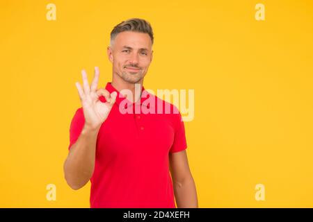 Alles ist OK. Schöner Mann zeigen OK gelben Hintergrund. Glücklicher Kerl lächeln mit Zufriedenheit. Einverstanden und akzeptabel. Vereinbarung und Genehmigung. Glücklich und zufrieden sein, Platz kopieren. Stockfoto