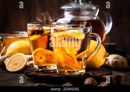 Winter oder Herbst heißen Heiltee mit Ingwer, Honig, Zitrone und Gewürzen in Glas Tasse mit Dampf, rustikalen Holzhintergrund Stockfoto