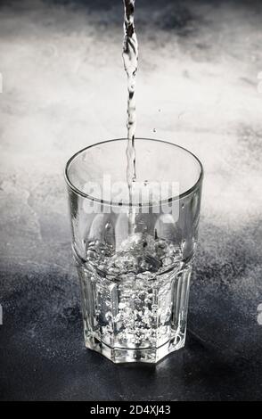 Die letzten Tropfen reinen Wassers werden in eine große Glasschale auf grauem Tischhintergrund gegossen, selektiver Fokus Stockfoto