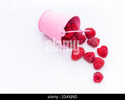 Rote reife Himbeeren fallen aus einem rosa Eimer auf weißem Hintergrund. Stockfoto