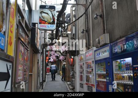 Tokio, Japan-2/24/16: In einer Gasse in Shinjuku macht sich ein Patrouillenmann auf den Weg. An den Seiten sehen wir verschiedene japanische Automaten. Stockfoto