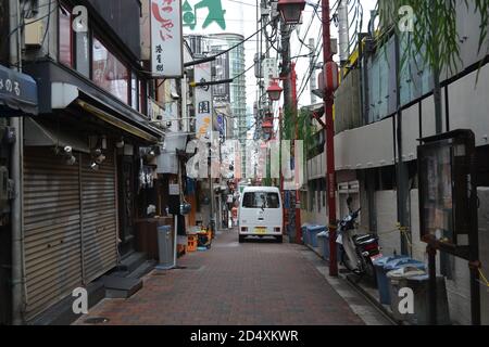 Tokio, Japan-2/24/16: Kleiner japanischer Van fährt eine verdichtete Gasse in Tokio mit verschiedenen Restaurants, Lebensmittelketten und Geschäften an der Seite. Stockfoto