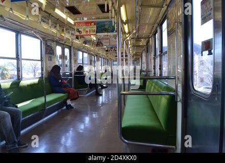 Itasbashi, Japan-2/25/16: In einem halb leeren japanischen Zug, der von Itabashi aus fährt; die Passagiere sitzen weit auseinander auf den grünen Sitzen. Stockfoto