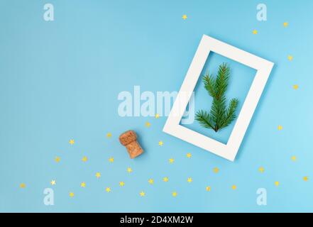 Blauer Hintergrund mit einem Sektflaschenkorken, einem weißen Rahmen und goldenem Konfetti in Sternform Stockfoto