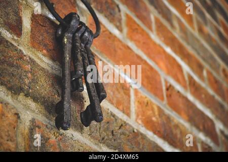 Ein Bündel alter antiker Schlüssel, die an einer modernen spitzen roten Ziegelwand hängen, neues Hauskonzept Stockfoto